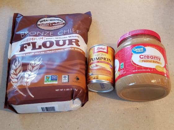 Whole wheat flour, a can of pumpkin puree, and a container of peanut butter.