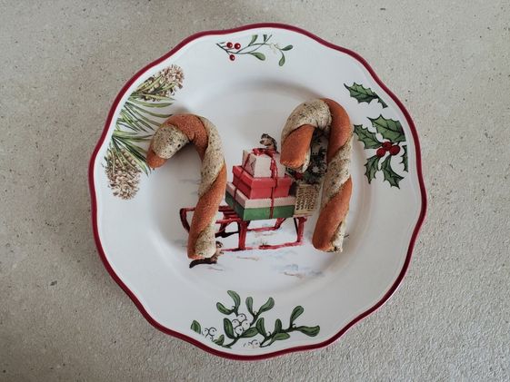 Two candy cane dog treats on a decorative Christmas plate.