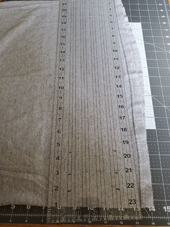 A t-shirt laid out on a cutting mat with a clear ruler on top ready to have the hem cut off.