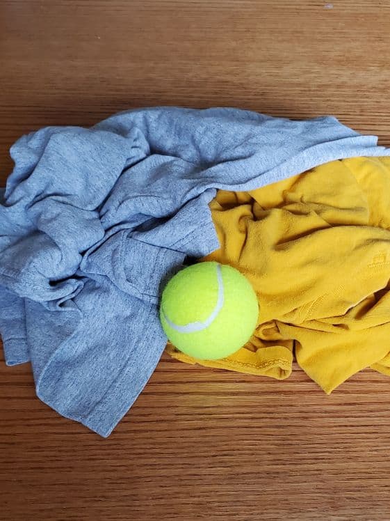 Two t-shirts and a tennis ball in a pile.