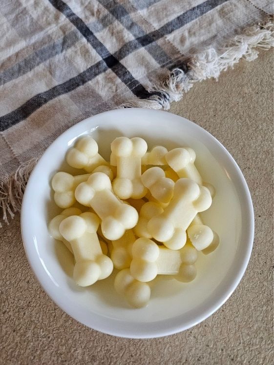 Bone shaped pineapple frozen dog treats in a white bowl next to a linen towel.