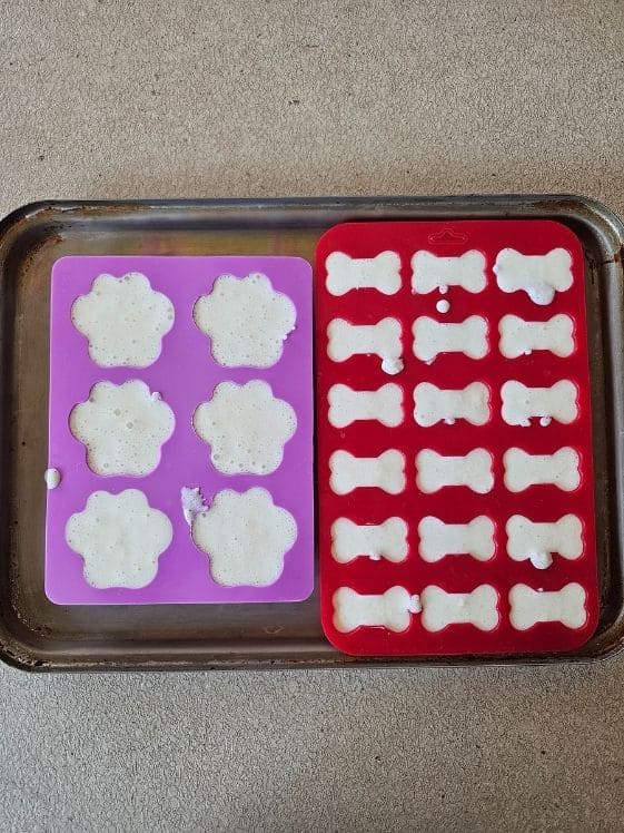 Paw and bone shaped silicone molds filled with the treat mixture.