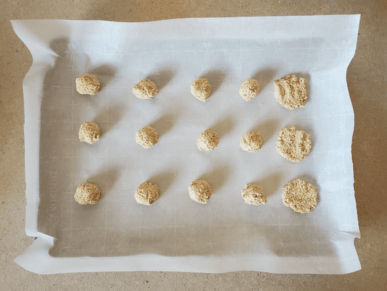 Oatmeal applesauce balls on a baking sheet. One row have been flattened.