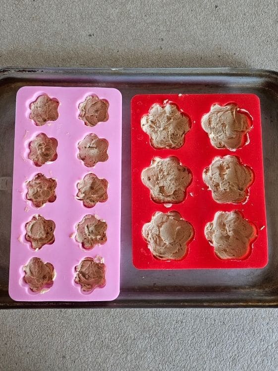 Paw shaped silicone molds filled halfway full with peanut butter yogurt mixture that has been pressed into the mold.