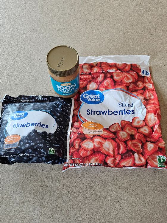 A bag of frozen blueberries, a bag of frozen strawberries, and a jar of natural peanut butter.