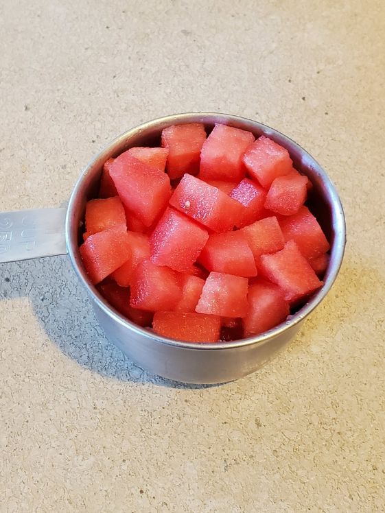 A measuring cup of watermelon chopped into small pieces.