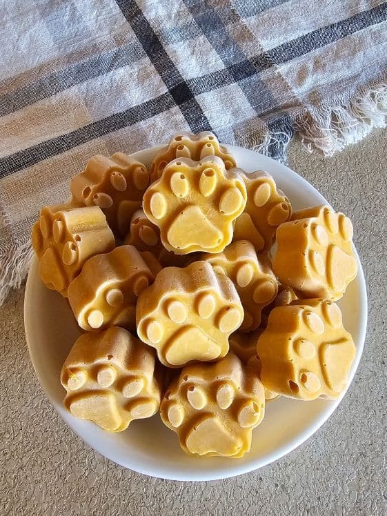 Paw shaped frozen peanut butter pumpkin dog treats in a white bowl next to a linen towel.