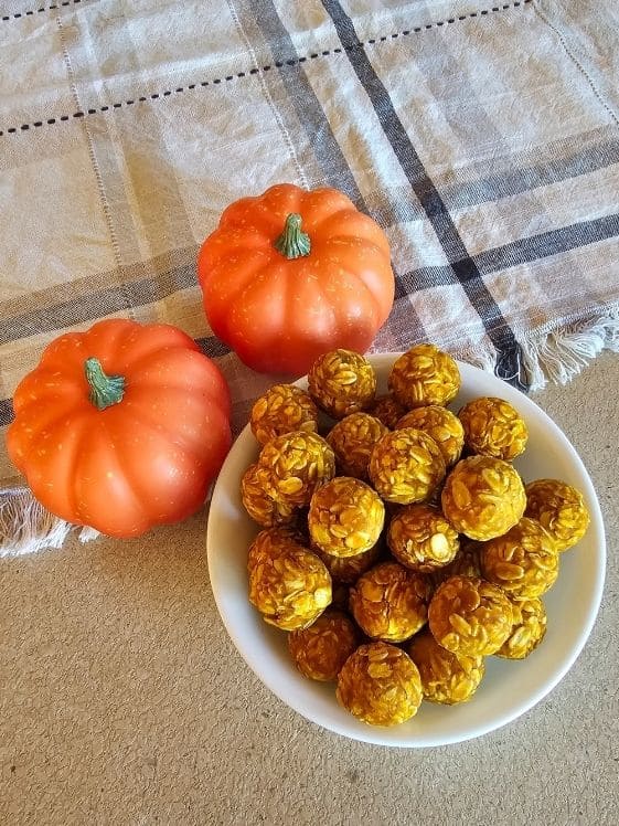 Peanut butter pumpkin dog treat balls in a bowl next to two small pumpkins and a linen towel.