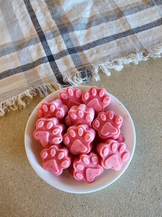 Paw shaped strawberry pineapple frozen dog treats in a bowl next to a linen towel.