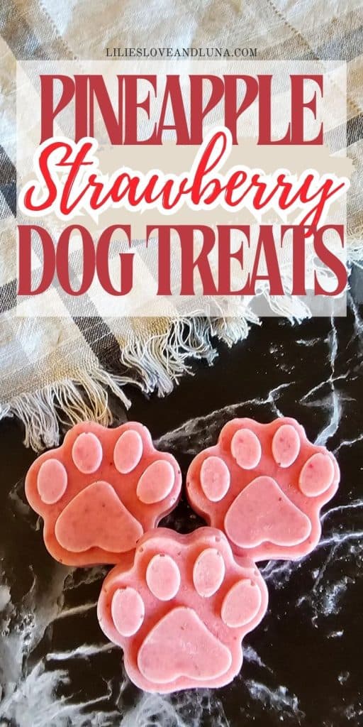 Three paw-shaped frozen dog treats in pink, featuring a mix of pineapple and strawberry flavors, are displayed on a dark surface with a textured background.