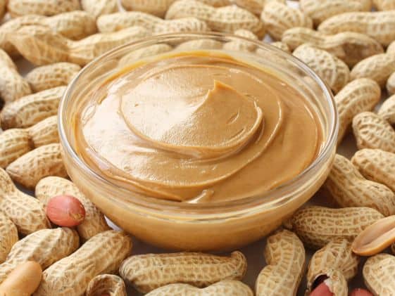 A bowl of peanut butter on top of a bunch of peanuts still in their shells.