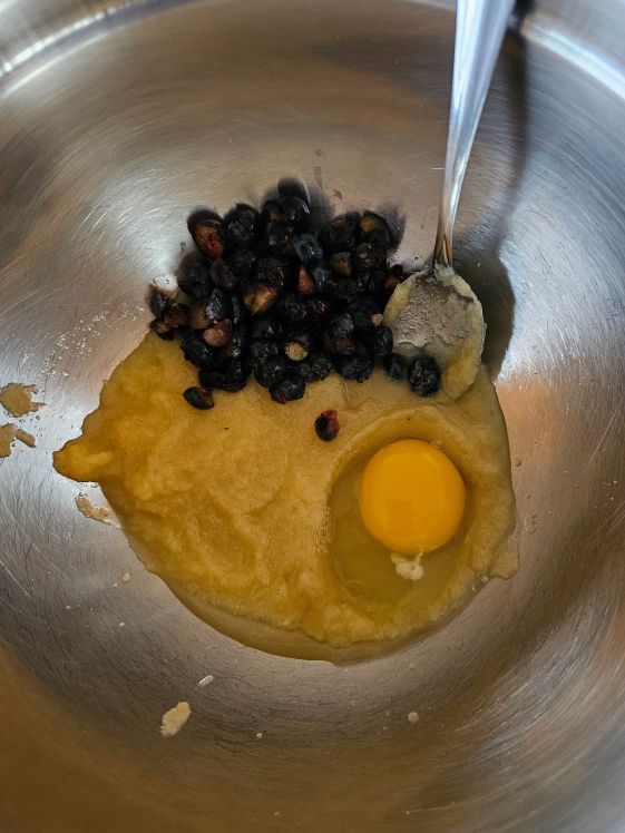 Applesauce, chopped blueberries, and an egg in a mixing bowl with a spoon.