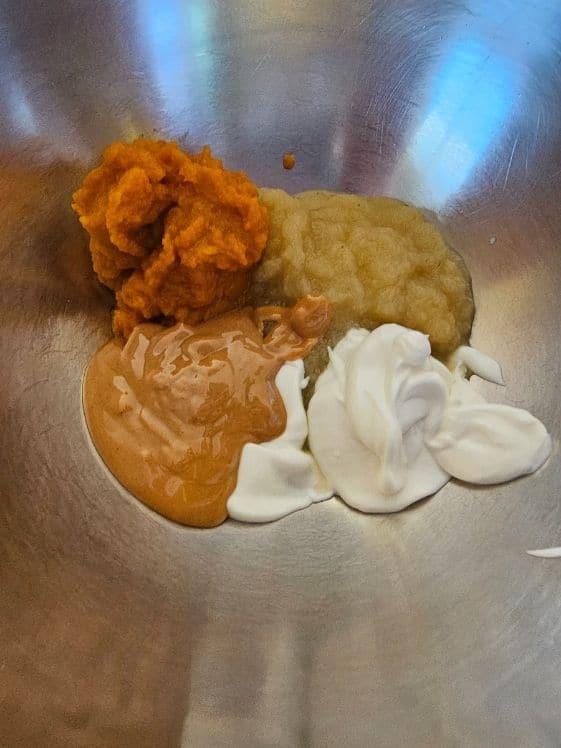 Pumpkin, applesauce, peanut butter, and Greek yogurt in a mixing bowl.