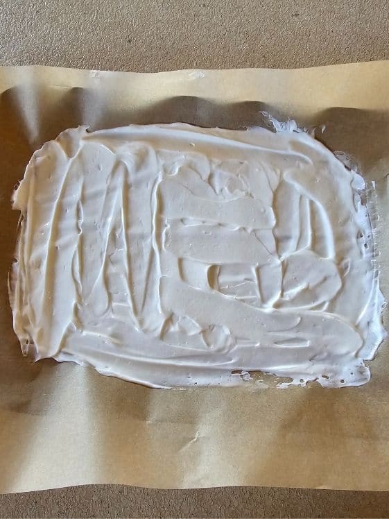 Yogurt spread out on a parchment paper lined cookie sheet.
