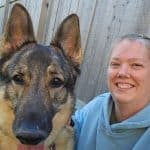 A German Shepherd next to a woman in a blue hoodie.