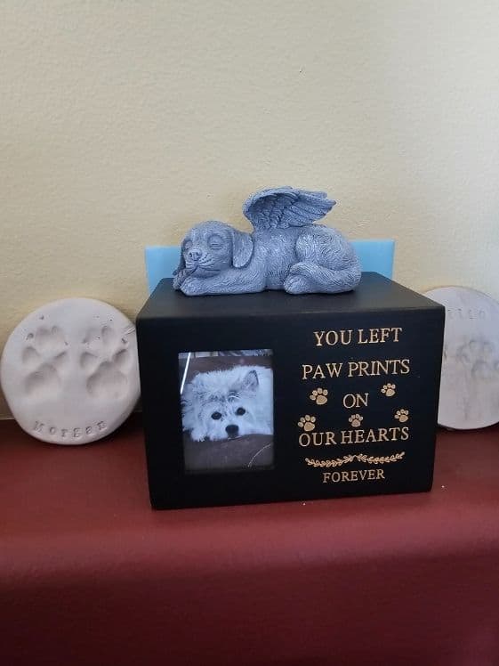 An urn for a dog next to a clay pawprint keepsake.