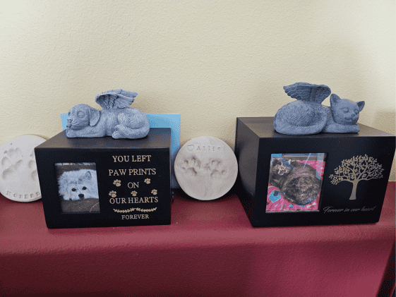 Two pet urns, one for a dog, one for a cat, with clay paw prints next to them.