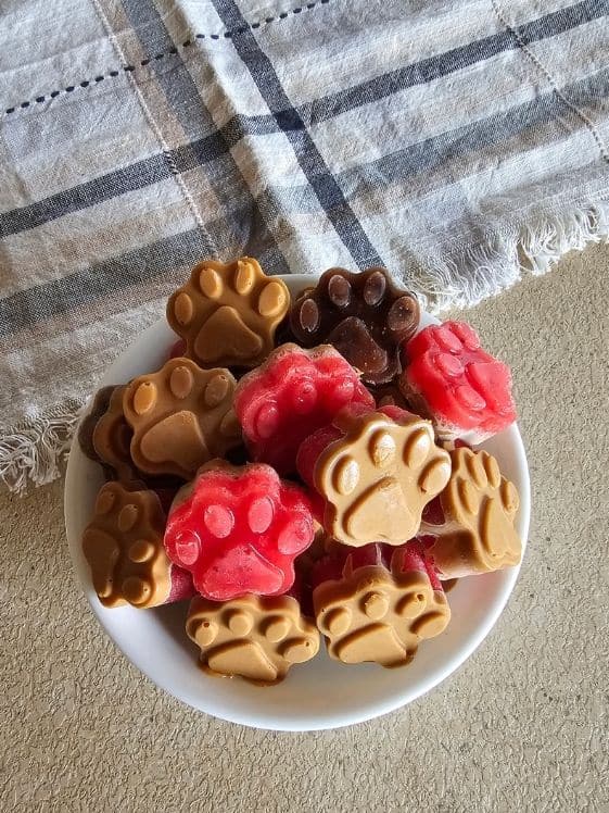 Paw shaped frozen dog treats in a bowl next to a linen towel.