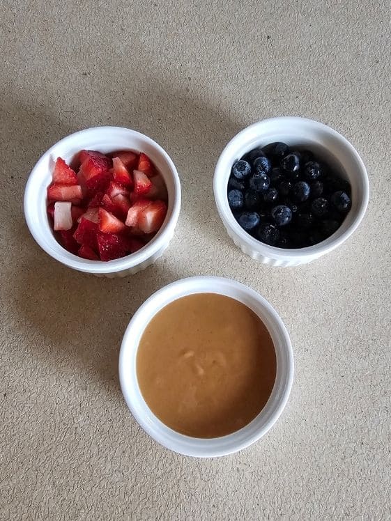 Chopped strawberries, blueberries, and peanut butter in individual white bowls.