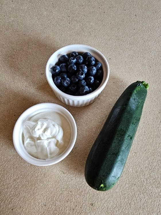 Blueberries and Greek yogurt in individual white bowls next to a small zucchini.