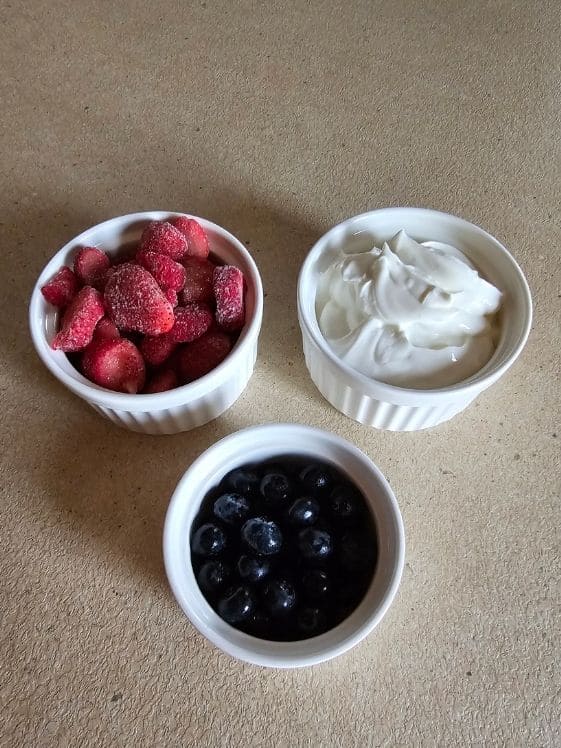 Strawberries, Greek yogurt, and blueberries in individual white bowls.
