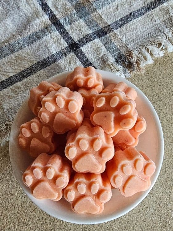 Paw shaped strawberry mango ice cream for dogs in a white bowl next to a linen towel.