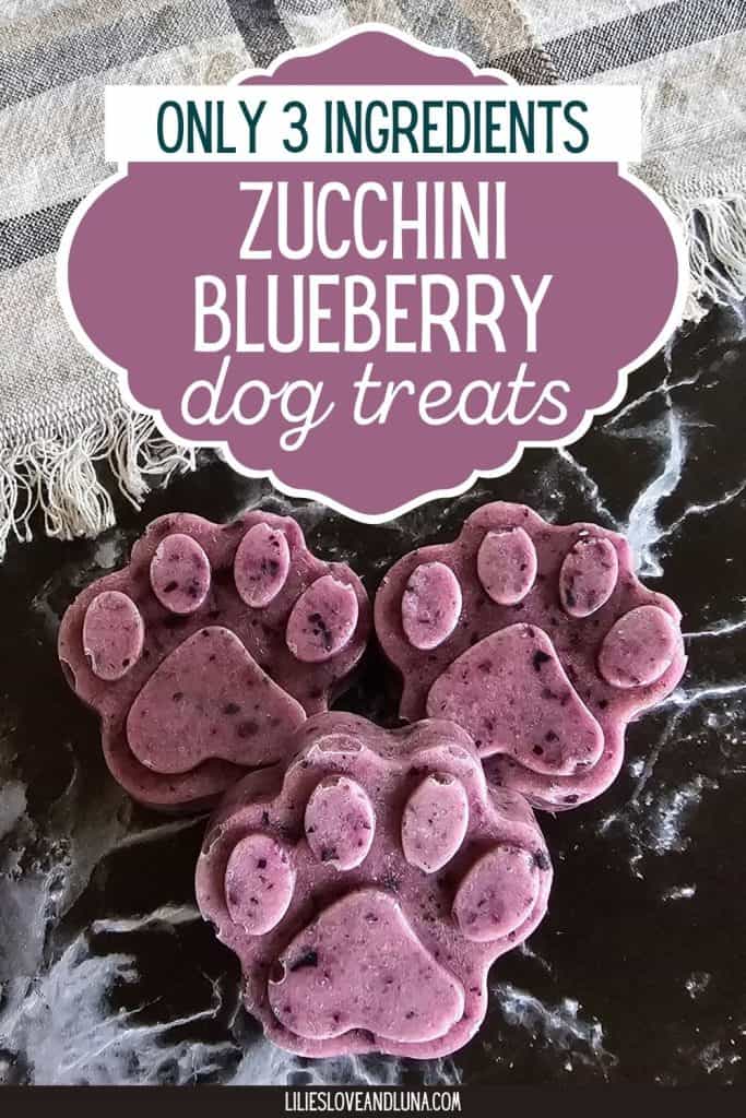 Homemade zucchini blueberry dog treats shaped like paw prints, made with only three ingredients, are displayed against a dark surface.