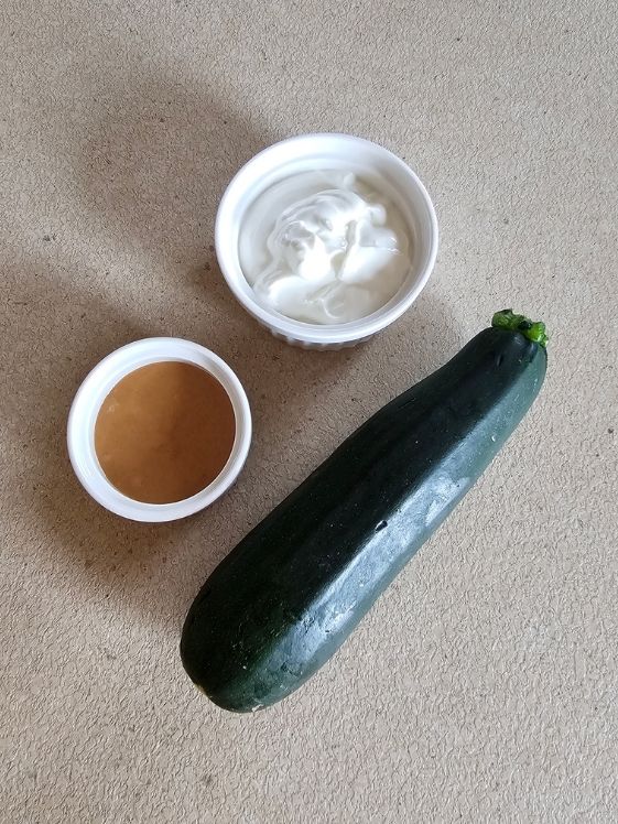 Greek yogurt and peanut butter in individual white bowls next to a whole zucchini.