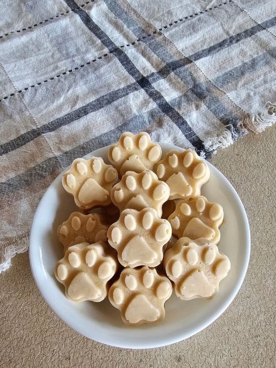 Paw shaped peanut butter zucchini icy bites in a white bowl next to a linen towel.