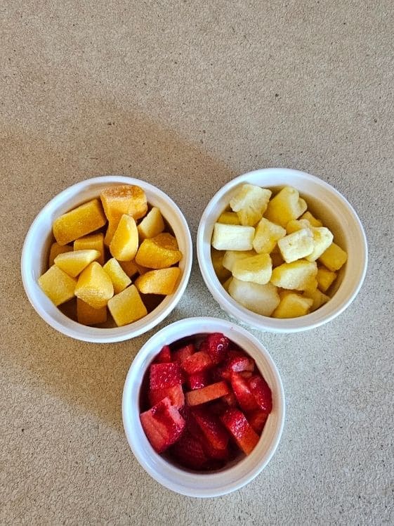 Mango, pineapple, and strawberry pieces in individual white bowls.