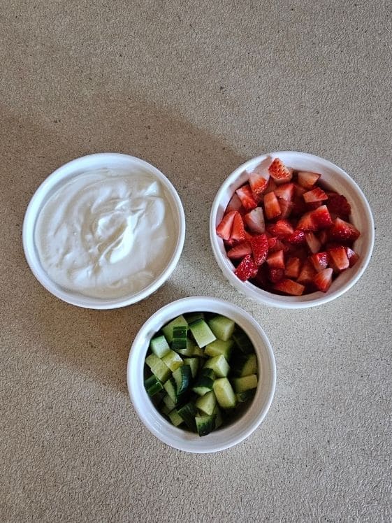 Greek yogurt, chopped strawberries, and chopped cucumber in individual white bowls.