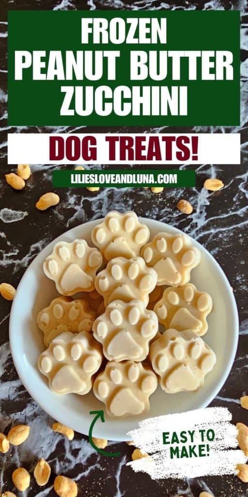 A plate of frozen peanut butter and zucchini dog treats shaped like paw prints is displayed on a marbled surface, accompanied by scattered peanuts.