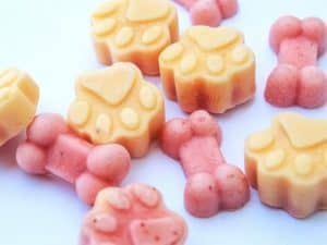 Paw and bone shaped frozen dog treats on a light surface.