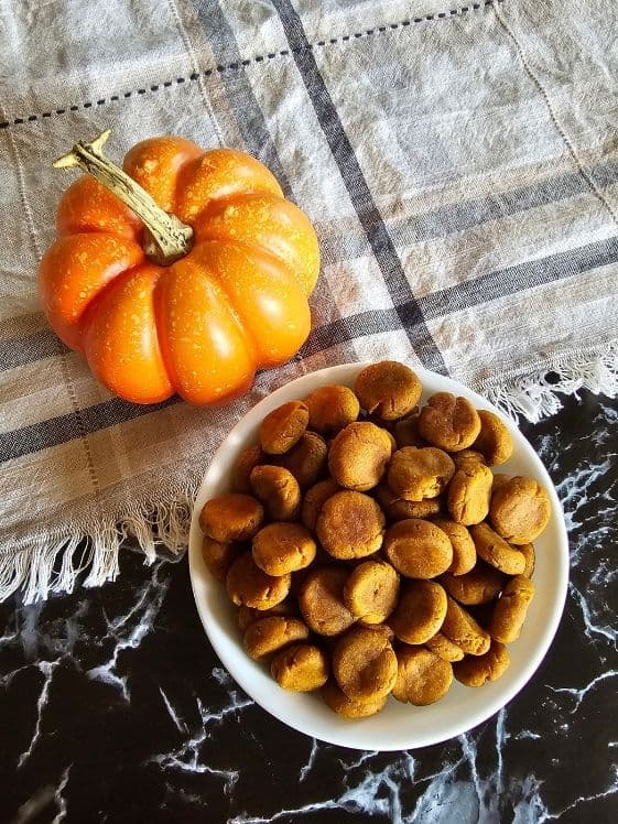 A bowl of soft baked peanut butter pumpkin dog treats next to a small pumpkin and a linen towel.