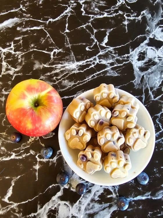 An apple next to a bowl of paw shaped frozen applesauce dog treats.