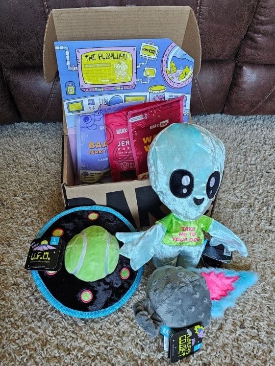 An open BarkBox showing alien themed dog toys and 3 bags of dog treats.