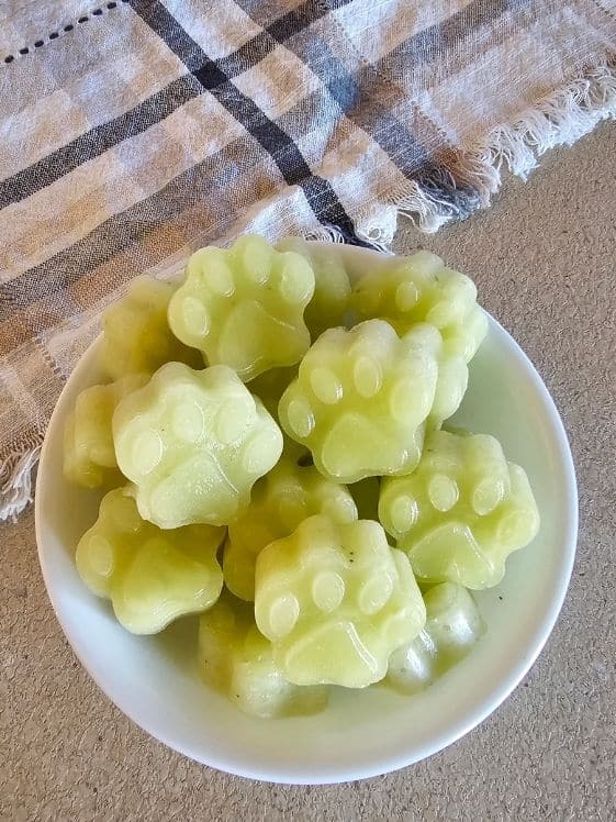 Paw shaped frozen tropical pup pops in a white bowl next to a linen towel.