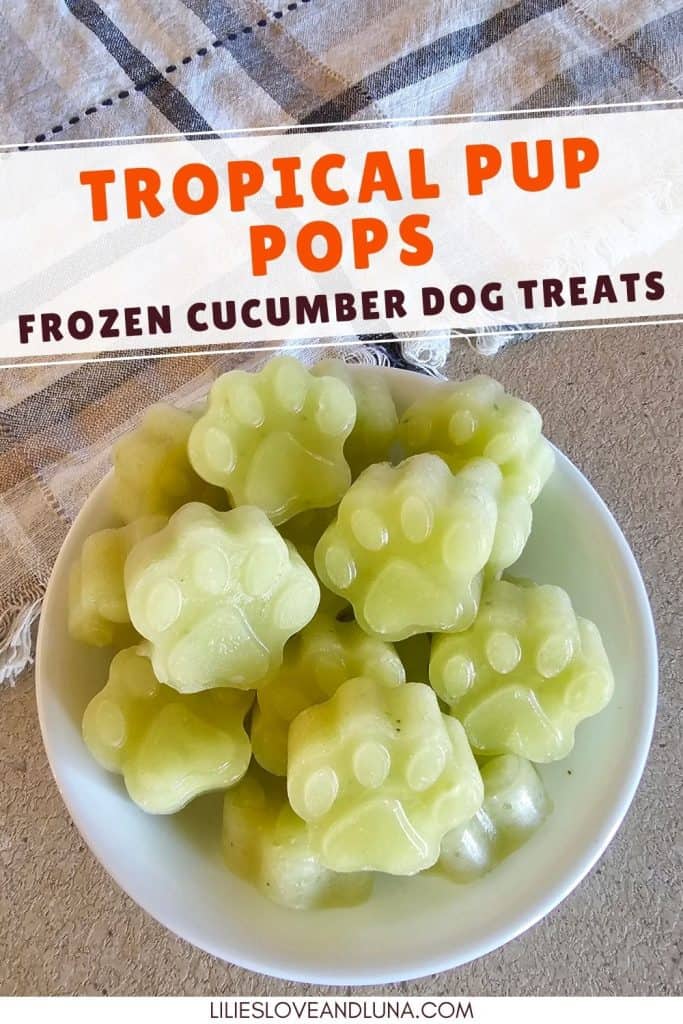 Bowl of green paw-shaped frozen dog treats made with cucumber, pineapple, and banana, displayed on a light-colored surface with the text "Tropical Pup Pops Frozen Cucumber Dog Treats."